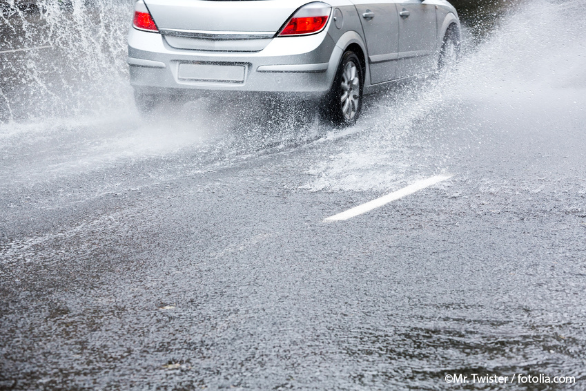 Mit Wasser überflutete Straße, auf der ein fahrendes silbergraues Auto Spritzwasser erzeugt. Bildquelle Mr. Twister / fotolia.com