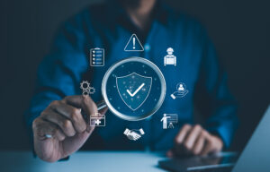 Mann hält Lupe mit Symbolen für Arbeitssicherheit, Compliance, Risikomanagement und betriebliche Effizienz. Bildquelle: Supatman -stock.adobe.com